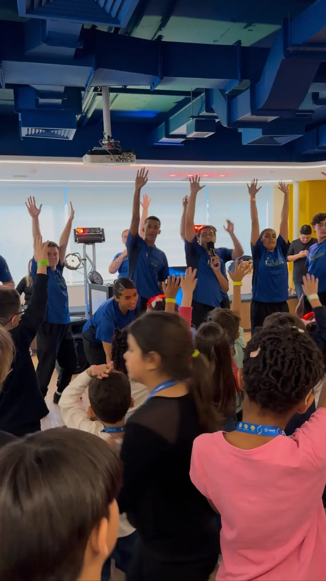 Crianças com as mãos levantadas acompanhando recreadores durante atividade coletiva em Kids Day