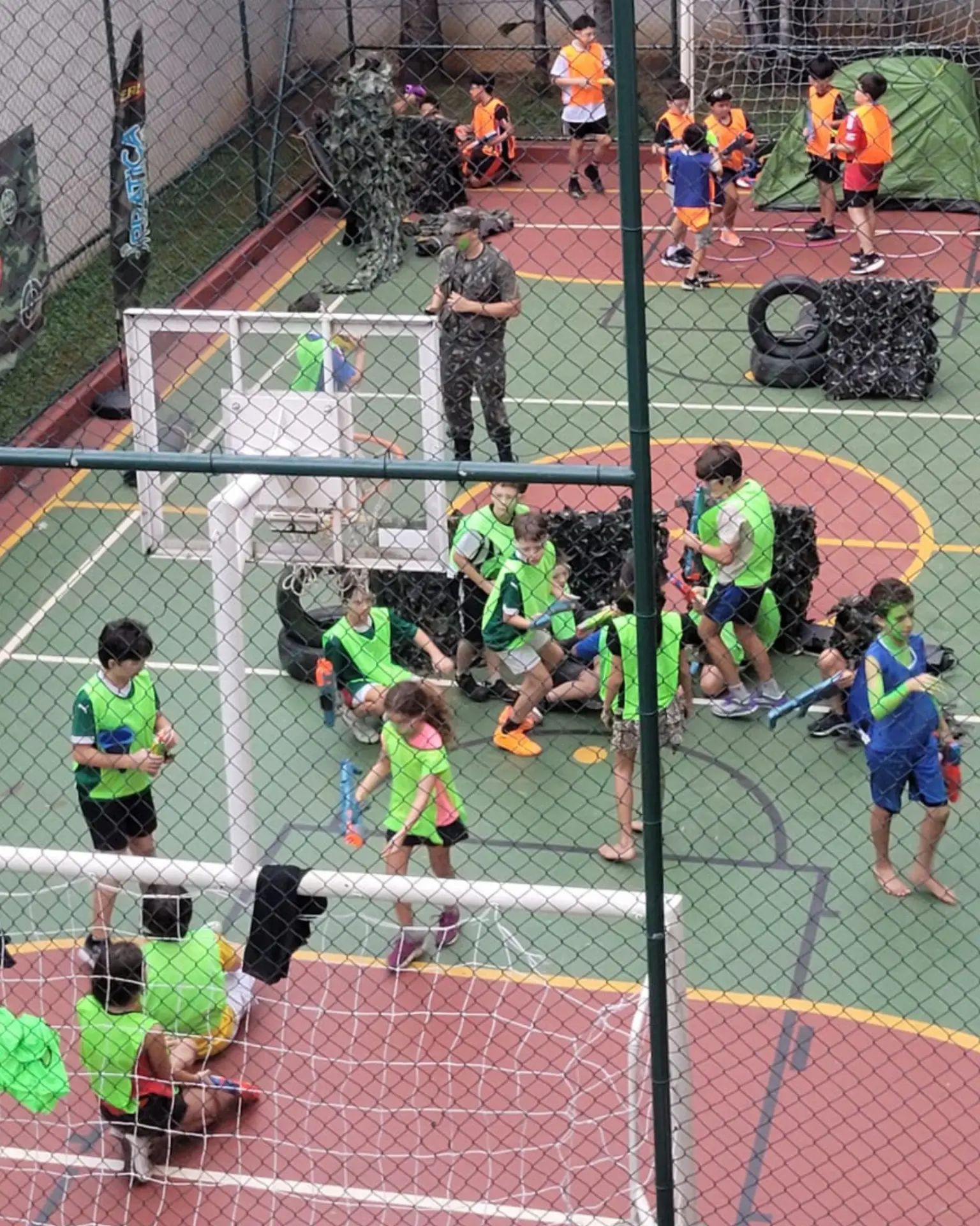 Arena Nerf montada em quadra, com crianças divididas em equipes de coletes coloridos durante a festa