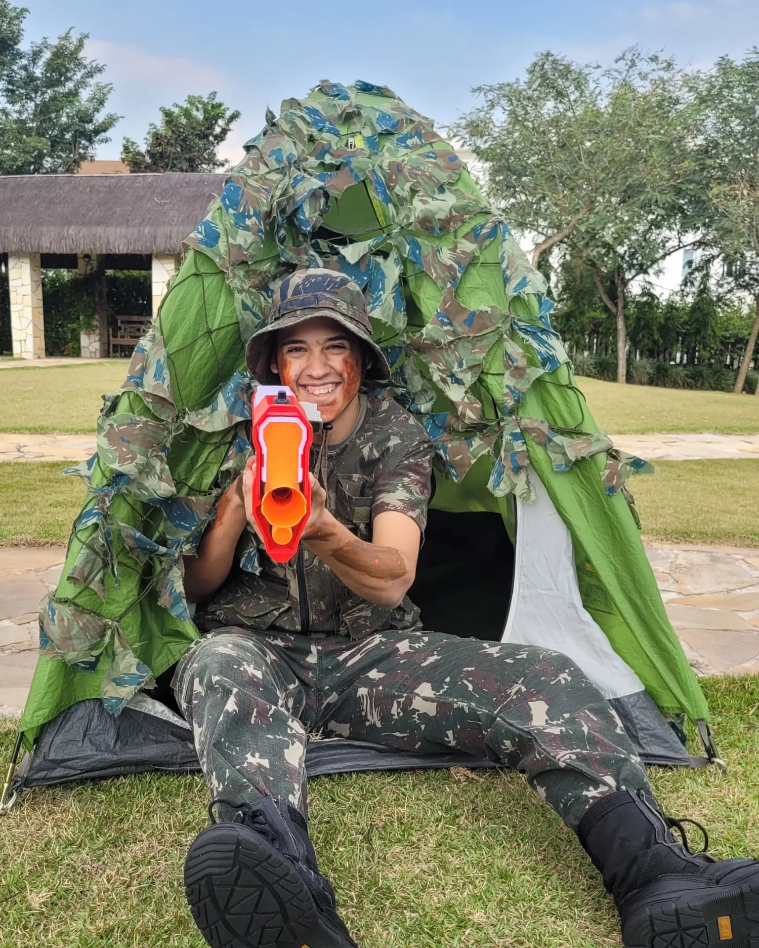 Recreador caracterizado com camuflagem e lançador Nerf na entrada da barraca da arena