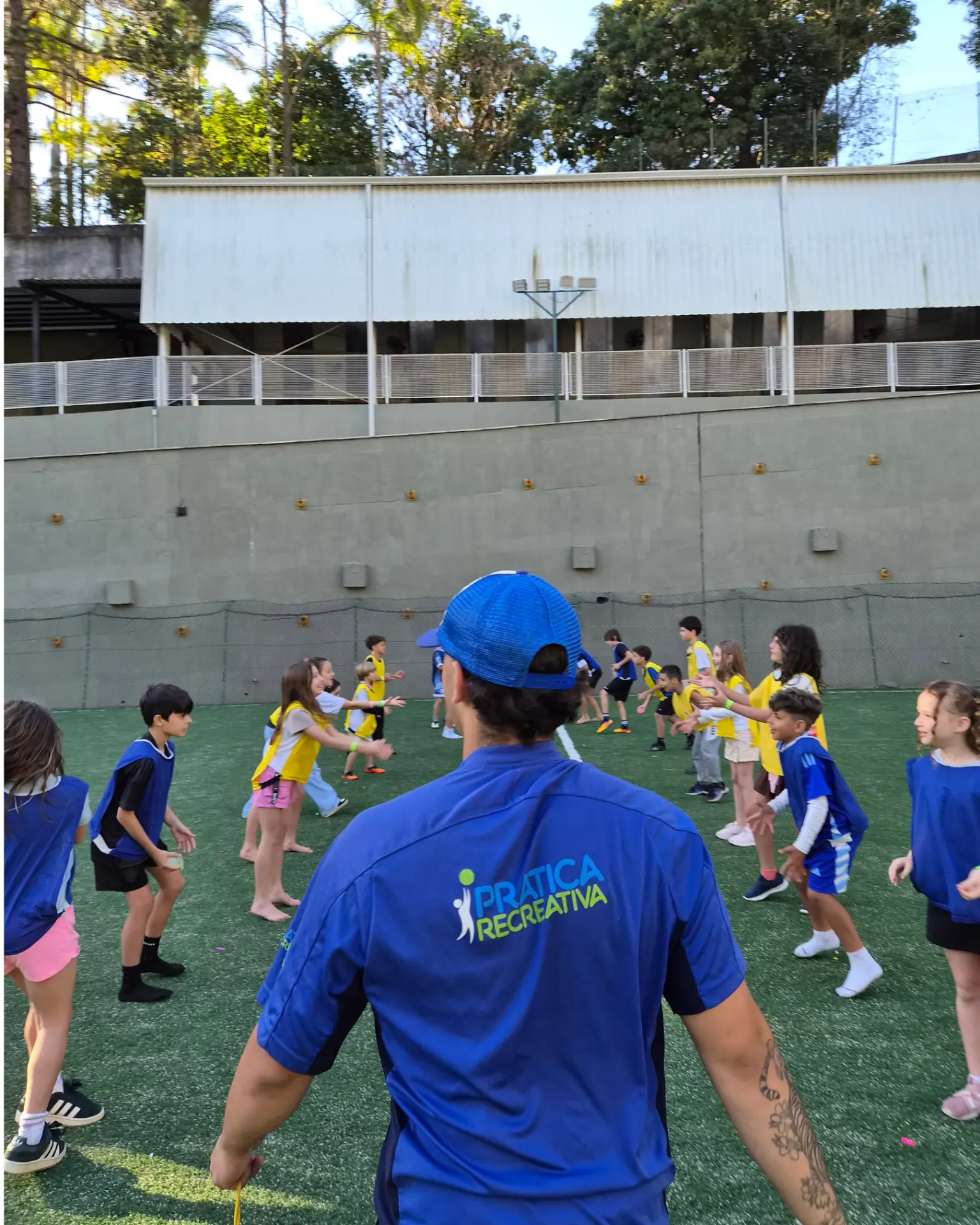 Recreador de camiseta azul da Prática Recreativa brincando com crianças de coletes na quadra de um condomínio