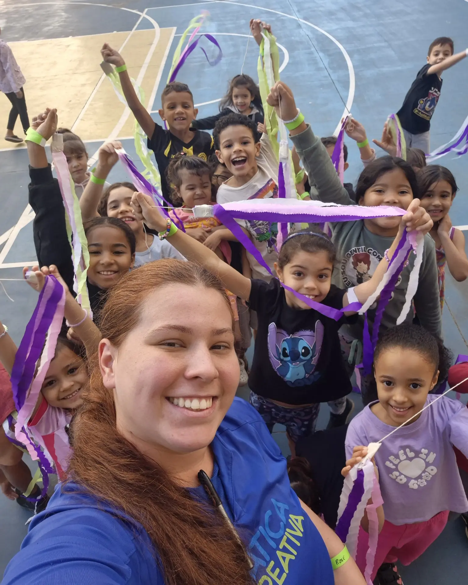 Recreadora da Prática Recreativa e crianças erguendo fitas coloridas durante atividade em evento