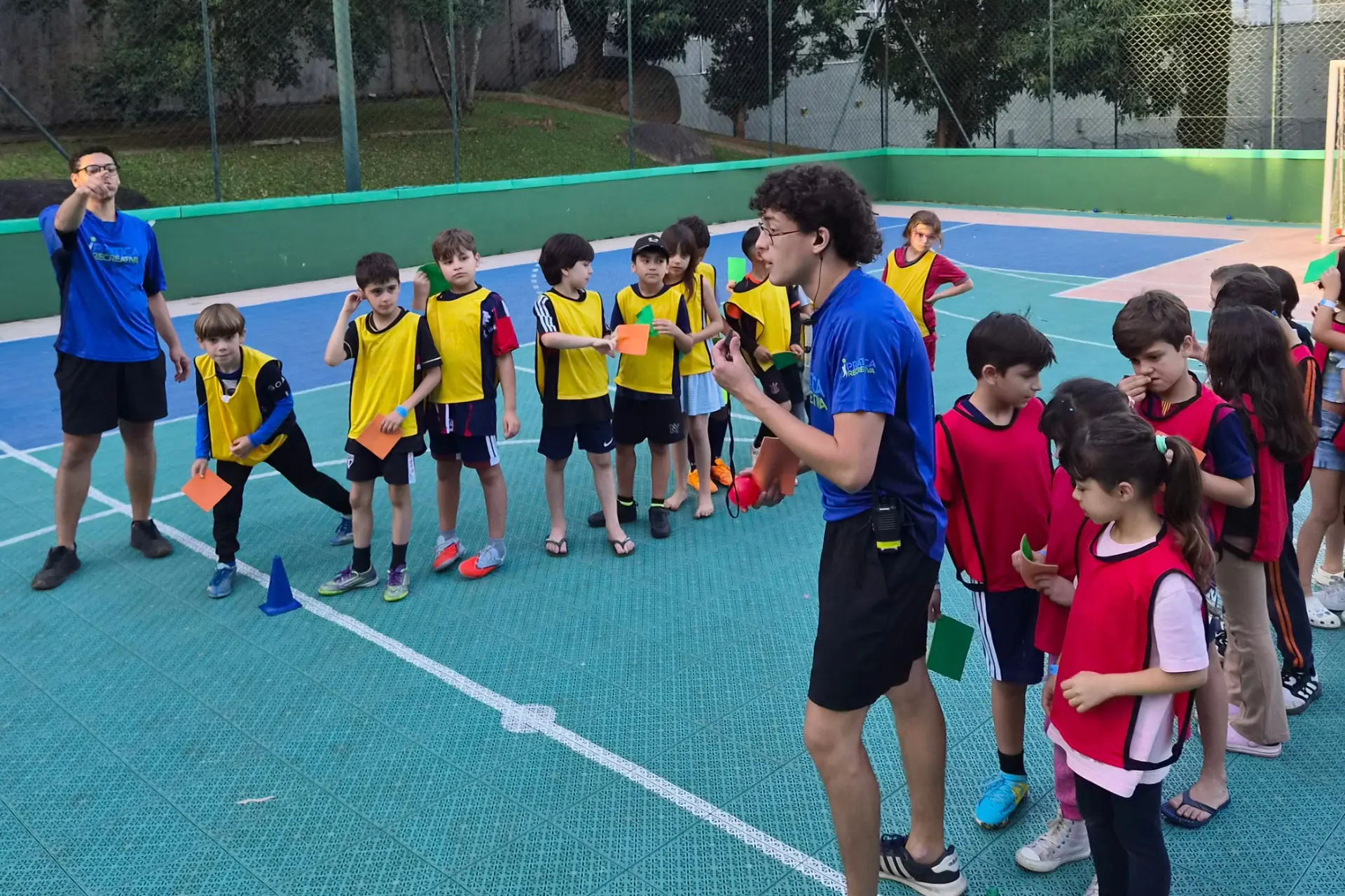 Crianças de coletes coloridos reunidas com recreadores antes de uma atividade esportiva