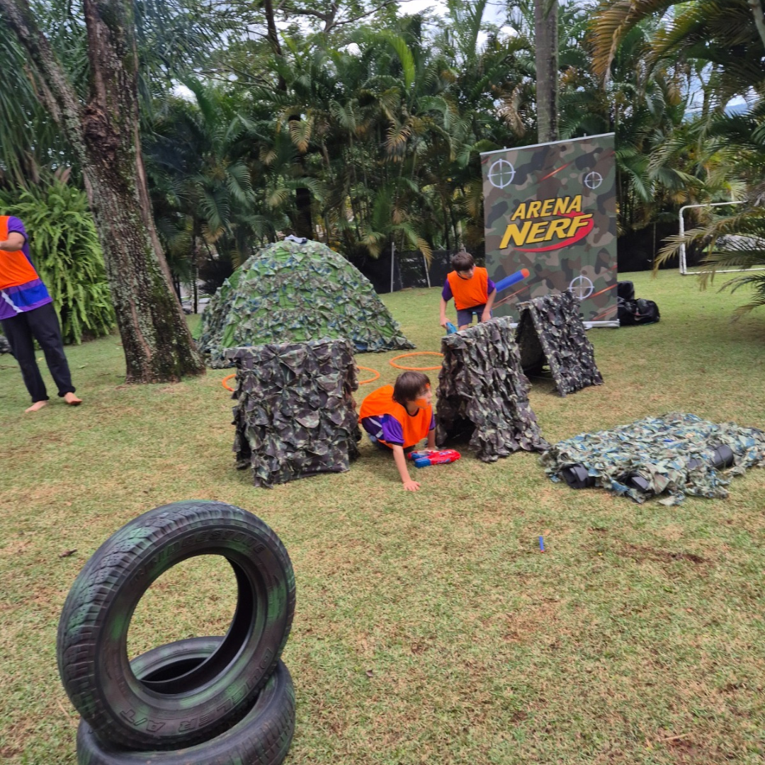 Crianças atravessando obstáculos com rede de camuflagem na Arena Nerf montada em área externa