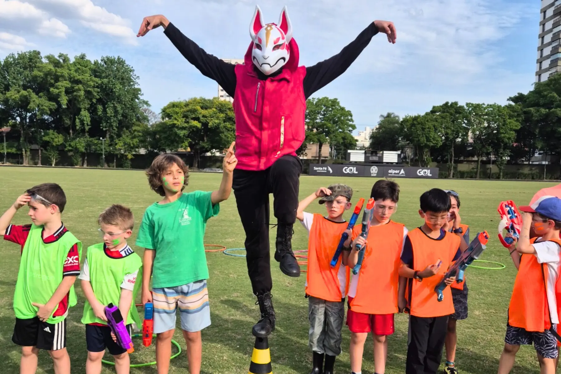 Recreação Nerf conduzida pela equipe da Prática Recreativa em campo, com recreador mascarado saltando entre as crianças