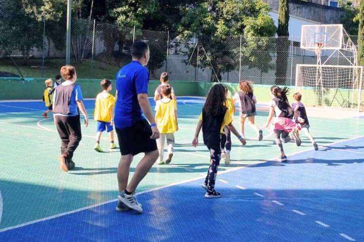 Crianças em atividade esportiva em quadra com recreador
