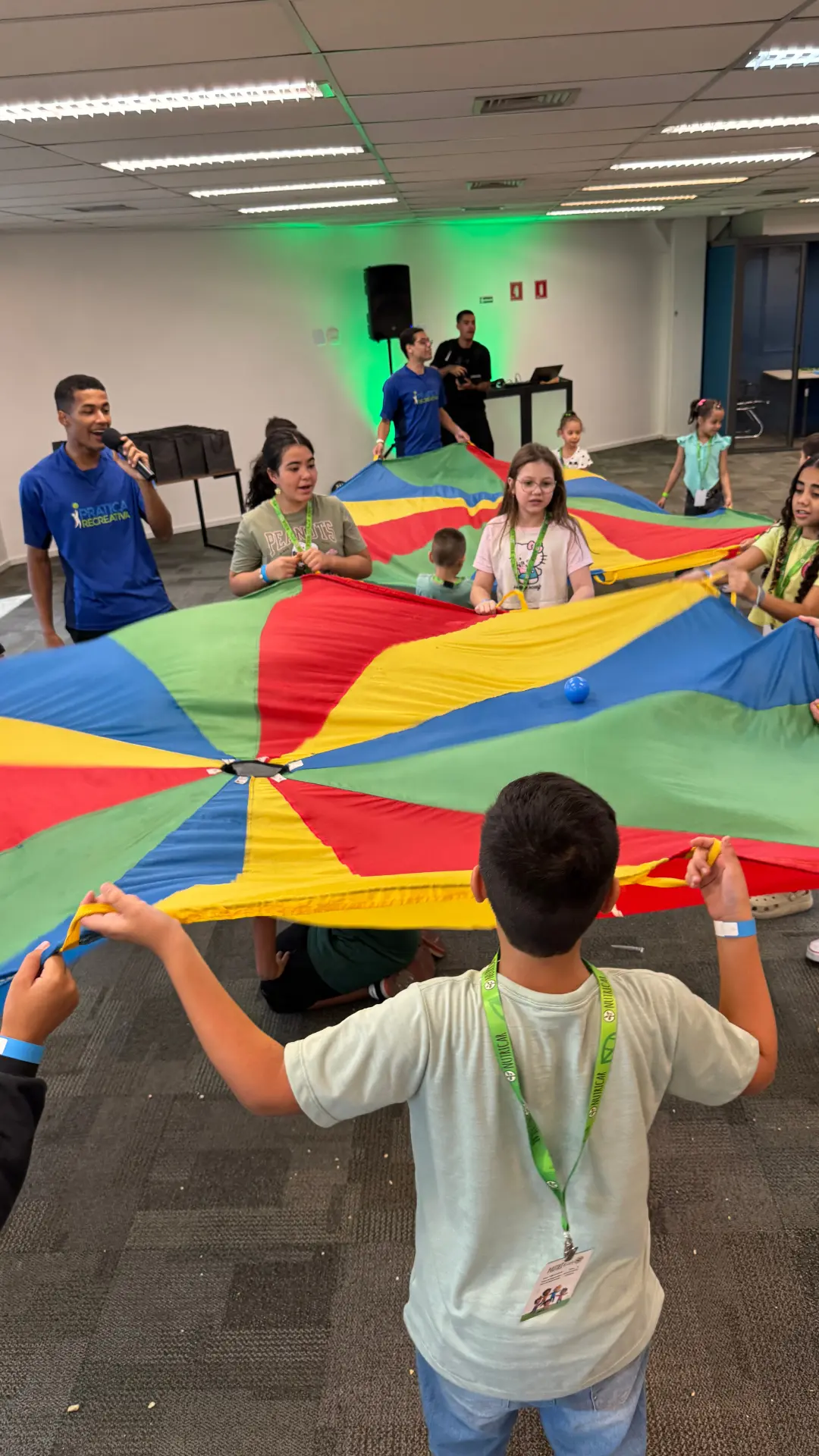 Crianças e recreadores segurando um paraquedas colorido durante recreação para filhos de colaboradores