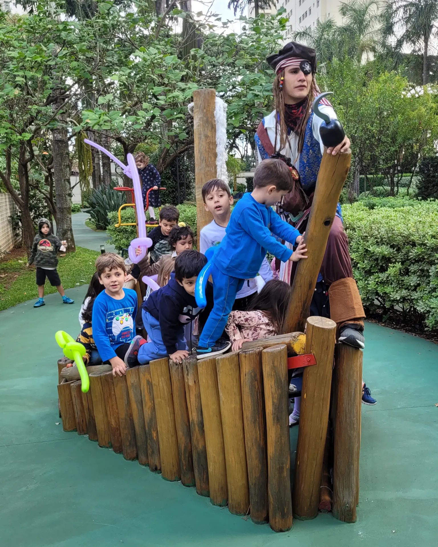 Recreador fantasiado de pirata brincando com crianças em barco de madeira durante festa infantil